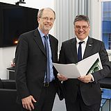Zwei Personen stehen nebeneinander vor einem Fernseher