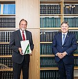 Eine Person hält ein Zertifikat in der Hand und steht neben einer anderen Person