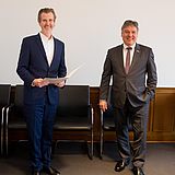 Person hält ein Dokument in der Hand und steht neben einer Person